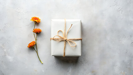 Simple white gift box tied with twine and delicate orange flowers on a textured gray background