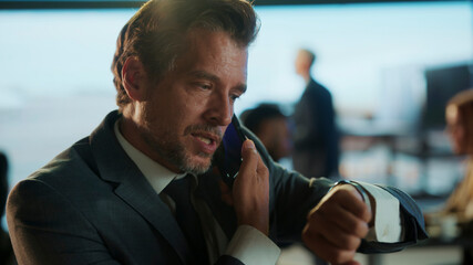 Businessman talking on phone and checking time in airport lounge