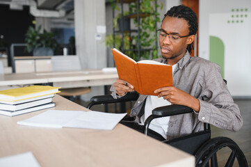 Focused african american student in wheelchair reading book in modern office