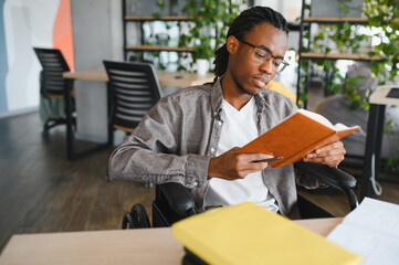 Obraz premium Focused african american student in wheelchair reading a book in modern office