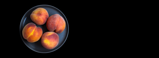 Four large whole round peaches on dark plate on black long background