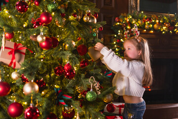 Merry Christmas Xmas holiday. Little girl decorating Christmas tree on Christmas eve at home. Young kid near classical Christmas tree with winter decorations ornaments. Time for celebration Christmas