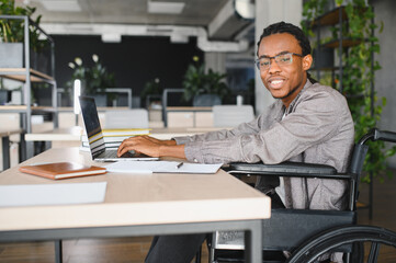 Young black freelancer in wheelchair working on laptop in modern office