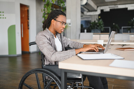 Fototapeta Focused african american employee using laptop in wheelchair at office desk