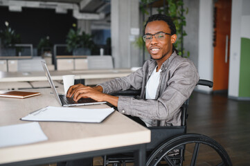 Confident african american freelancer working on laptop in wheelchair at modern office