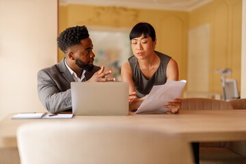 Serious businesswoman analyzing performance report with male financial advisor at desk in...