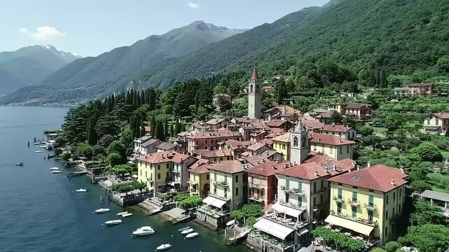 An aerial view showcases a charming lakeside village nestled amongst lush greenery and towering mountains. Red-roofed buildings line the waterfront, boats bob gently in the calm waters, and