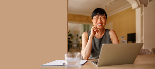 Portrait of happy entrepreneur analyzing online data over laptop while working in modern office against wall