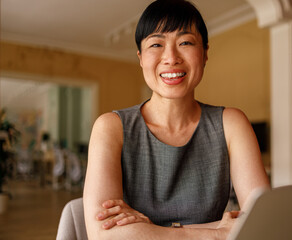 Portrait of confident female manager with arms crossed smiling at camera while working in modern office