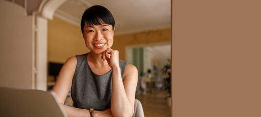 Portrait of smiling mid adult businesswoman with laptop on desk working in modern corporate workplace