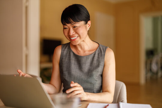 Mid adult businesswoman smiling and engaged in project planning on video conference call over laptop in corporate office - Powered by Adobe