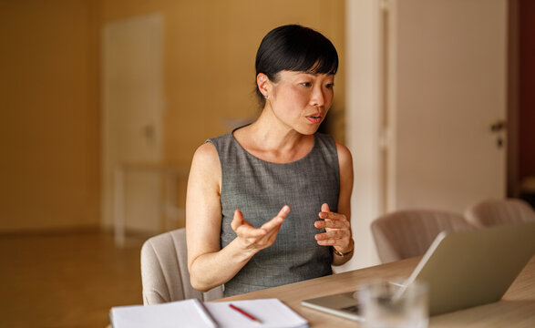 Portrait of serious professional woman discussing projects on video call using laptop at corporate desk