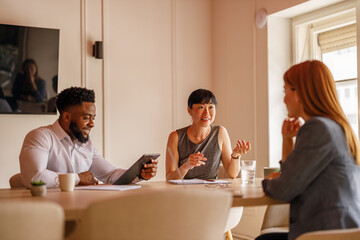 Business colleagues with digital tablet and documents sharing ideas in board room during office meeting