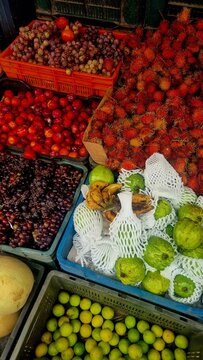 Colorful assortment of tropical fruits including guavas, limes, rambutans, bananas, grapes, and plums on display at a local market stall in Munnar, Kerala, India.