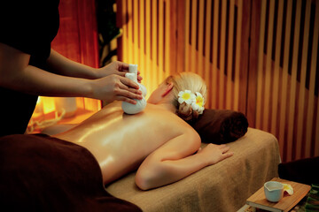 Hot herbal ball spa massage body treatment, masseur gently compresses herb bag on woman body....