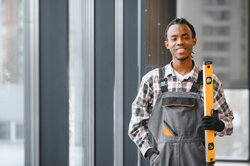 Young african american construction worker holding spirit level smiling by window