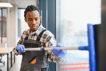 African American Professional cleaning service worker washing windows in office building
