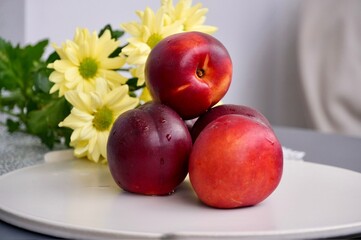 Ripe nectarines on a white plate with yellow chrysanthemums