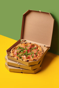 Delicious pizza with prosciutto and arugula in a delivery box on colorful background