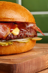 Delicious burger with bacon, cheese and pickles resting on wooden board