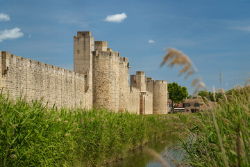 The Tour de la Poudrière and a section of the medieval city walls of Aigues-Mortes (Occitan: Aigasmòrtas), Gard, France, rise imposingly under a blue sky—ideal for themes of travel, history, heritage,