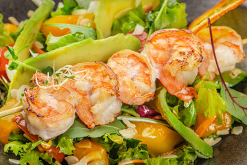 Grilled shrimp skewers rest atop a vibrant medley of fresh greens, ripe avocado, and colorful...