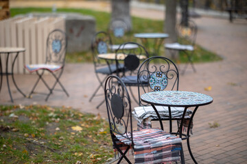 An outdoor cafe or restaurant patio with metal tables and chairs featuring colorful cushions, with...