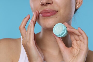 Young woman with lip balm on light blue background, closeup