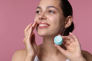 Young woman with lip balm on pink background