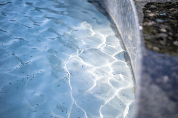 A close-up of a light blue water surface with shimmering light reflections in a city fountain,...