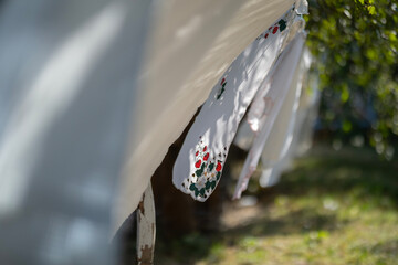 White tablecloths, some embroidered, hang to dry on a long clothesline with clothespins in a fruit...