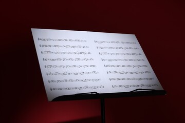 Note stand with music sheets on dark red background, closeup