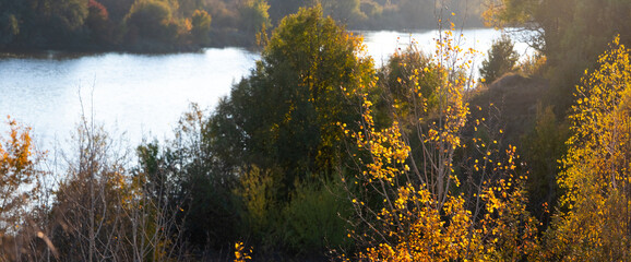 Autumn landscape with a river surrounded by trees and bushes with bright yellow foliage in the...