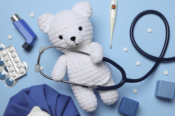 Pediatrics concept. Toy bear with stethoscope, thermometer and pills on light blue background, flat...