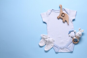 Baby clothes and accessories on light blue background, flat lay. Space for text