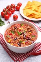 Tasty chili con carne in bowl, nachos and ingredients on grey table, closeup