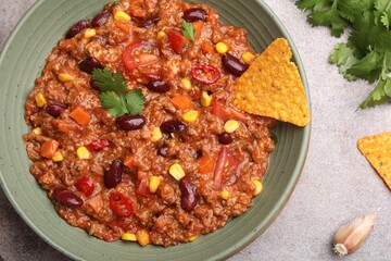 Tasty chili con carne in bowl and nachos on grey table, flat lay