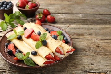 Tasty crepes with berries, cream and mint on wooden table, closeup. Space for text