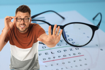 Man with eyesight problems, glasses and vision test chart on light blue background