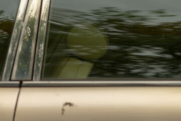 This is a detailed closeup image of a car window displaying a clear reflection of lush green trees...