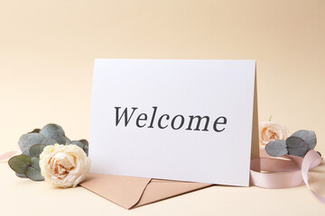 Welcome card, roses, eucalyptus branches and envelope on beige background