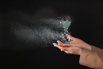 Time running out. Hourglass dissolving in woman's hands against black background, closeup