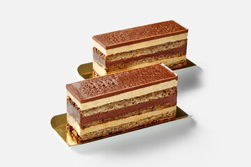 Two opera cakes with coffee and chocolate layers resting on golden trays