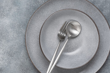 Two grey plates and silver cutlery on grey grunge background, top view