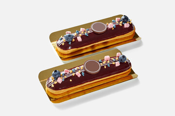 Two chocolate eclairs decorated with blueberries and sprinkles resting on golden trays