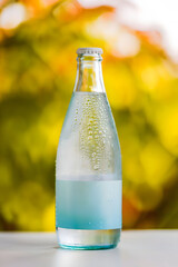 Chilled Clear Glass Bottle with Blank Label and Condensation Set Against Vibrant Yellow and Orange Blurred Outdoor Background