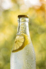 Close-Up of Chilled Glass Bottle with Lemon Slice and Condensation Droplets Against a Warm Yellow Bokeh Background