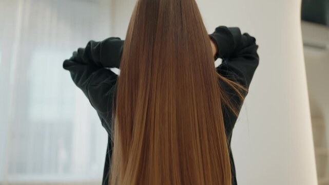 A woman with long, luxurious brown hair runs her fingers through it. She is facing away from the camera, highlighting the length and health of her hair. Modern Beauty Salon