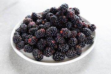 heap of fresh blackberries on white plate, side view
