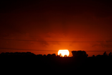 Sunset over the horizon with silhouetted trees and power lines in a tranquil landscape during the...